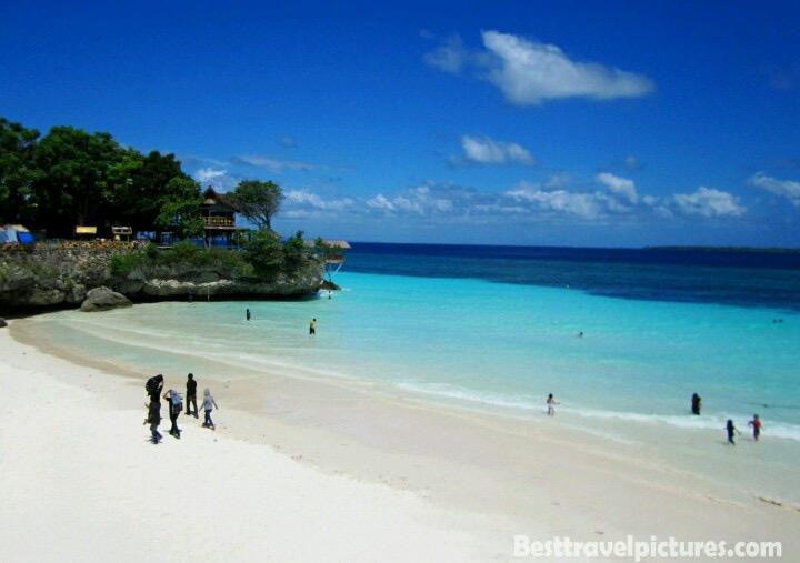 Pantai berpasir putih dengan pengunjung di tepi air.
