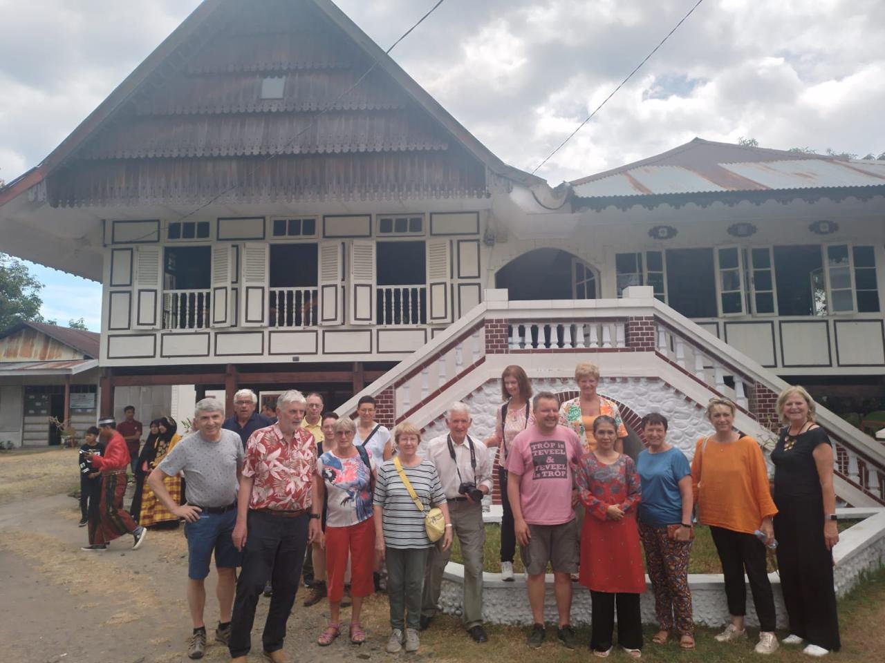 Rombongan pengunjung di depan rumah kayu berpanggung.