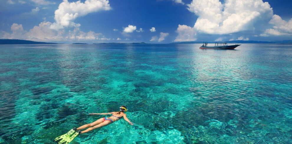 Perenang di permukaan laut jernih dekat perahu.