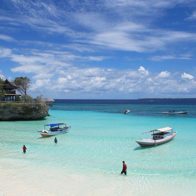Pantai berpasir putih dengan perahu di perairan dangkal.