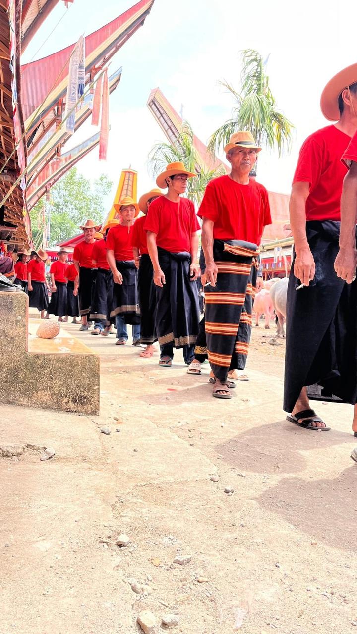 Barisan orang mengenakan pakaian merah dan hitam dalam kegiatan budaya.