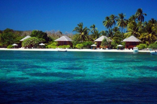 Pantai tropis dengan pondok dan pohon kelapa.