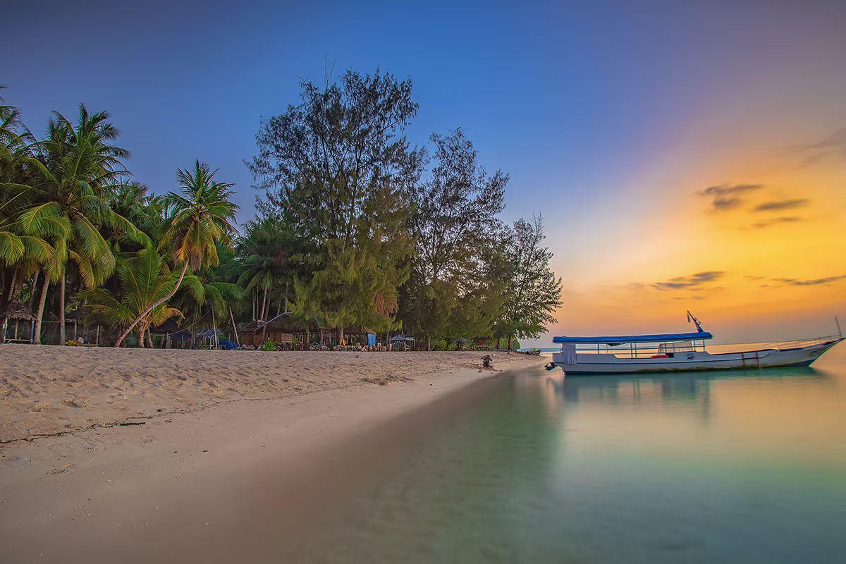 Perahu di tepi pantai saat matahari terbenam.